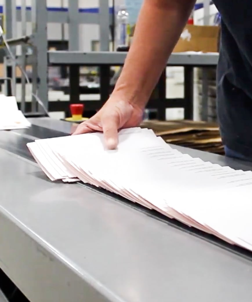 Production worker collecting folded print material on machine conveyor belt